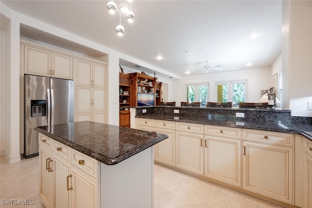 kitchen with a kitchen island, stainless steel refrigerator with ice dispenser, cream cabinets, and dark stone counters