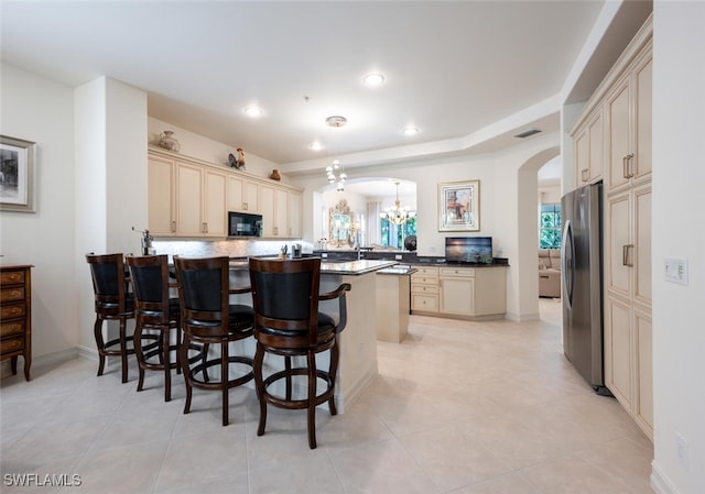 kitchen featuring light tile patterned floors, a breakfast bar, cream cabinets, and stainless steel refrigerator