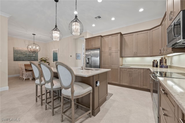 kitchen with stainless steel appliances, a center island with sink, sink, light stone countertops, and decorative light fixtures