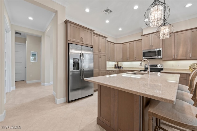 kitchen featuring a center island with sink, appliances with stainless steel finishes, light stone countertops, pendant lighting, and sink