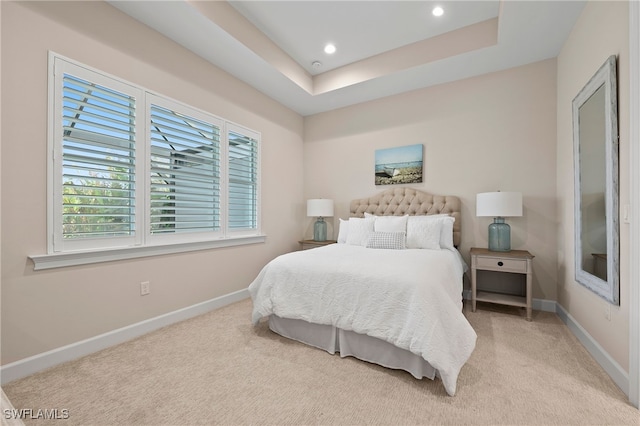 bedroom featuring light carpet, multiple windows, and a tray ceiling