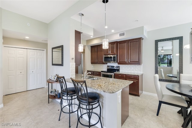 kitchen featuring light stone counters, kitchen peninsula, decorative light fixtures, decorative backsplash, and appliances with stainless steel finishes