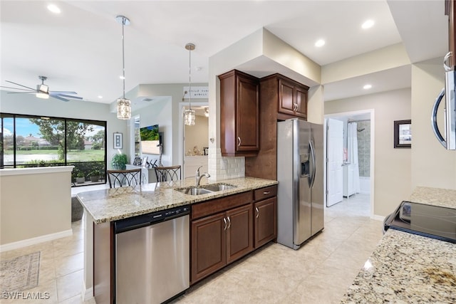 kitchen featuring appliances with stainless steel finishes, light stone counters, ceiling fan with notable chandelier, sink, and pendant lighting