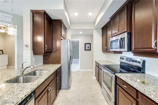 kitchen featuring light stone countertops, sink, hanging light fixtures, decorative backsplash, and appliances with stainless steel finishes