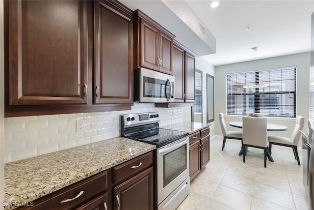 kitchen with light stone countertops, backsplash, decorative light fixtures, light tile patterned floors, and appliances with stainless steel finishes