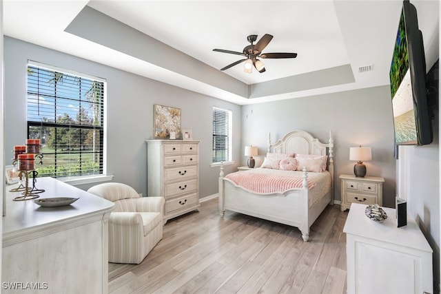 bedroom with a tray ceiling, ceiling fan, and light wood-type flooring