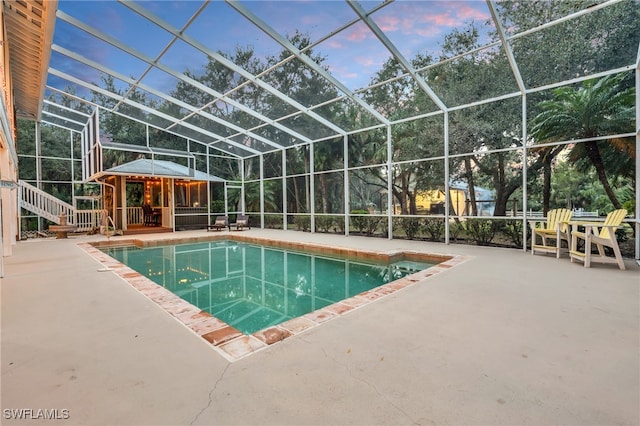 pool at dusk with a patio and glass enclosure