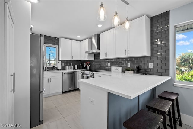 kitchen with kitchen peninsula, decorative backsplash, a breakfast bar, wall chimney exhaust hood, and stainless steel appliances