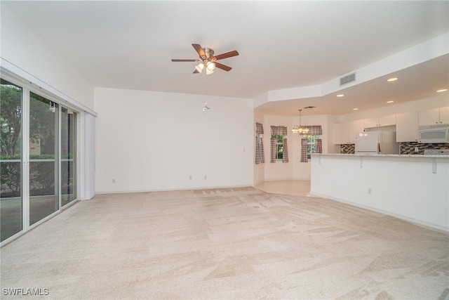 unfurnished living room with ceiling fan with notable chandelier and light colored carpet