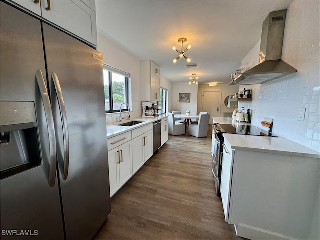 kitchen with appliances with stainless steel finishes, sink, wall chimney range hood, a notable chandelier, and white cabinets