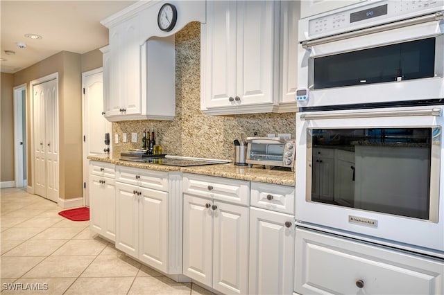 kitchen with tasteful backsplash, light stone counters, multiple ovens, light tile patterned floors, and white cabinetry