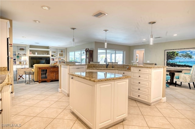 kitchen with a center island with sink, light stone counters, hanging light fixtures, and light tile patterned flooring