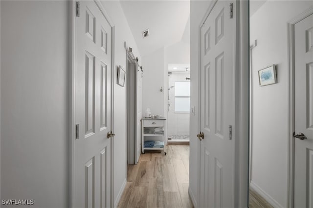 hall with light hardwood / wood-style floors, lofted ceiling, and a barn door