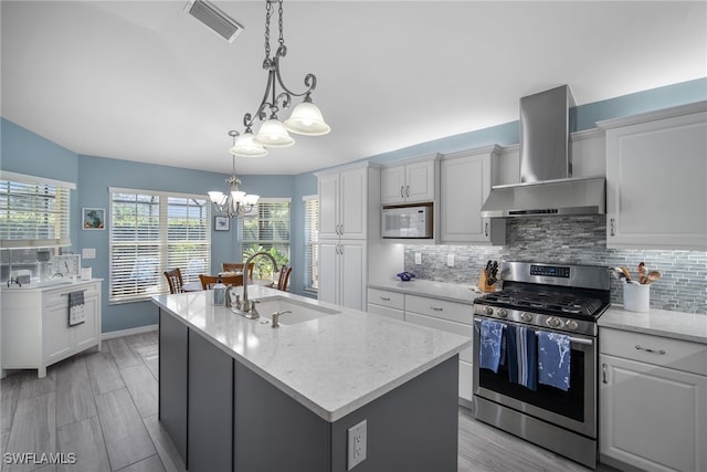 kitchen featuring wall chimney range hood, sink, an island with sink, gas stove, and white cabinetry