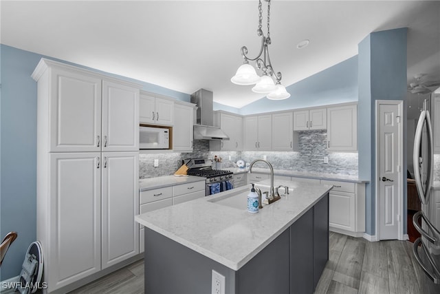 kitchen with wall chimney range hood, appliances with stainless steel finishes, white cabinetry, and a kitchen island with sink