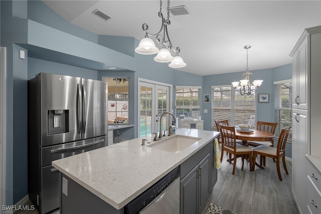 kitchen with a center island with sink, stainless steel appliances, sink, gray cabinetry, and decorative light fixtures