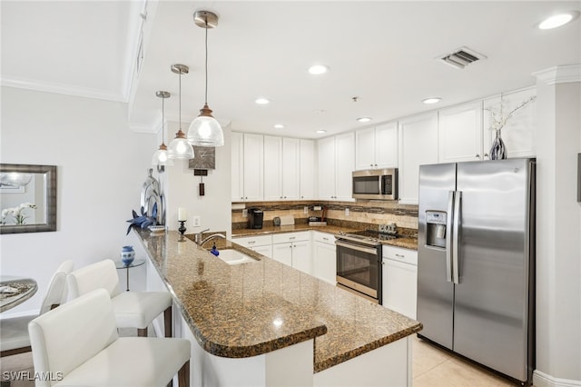 kitchen with stainless steel appliances, sink, dark stone counters, and decorative light fixtures