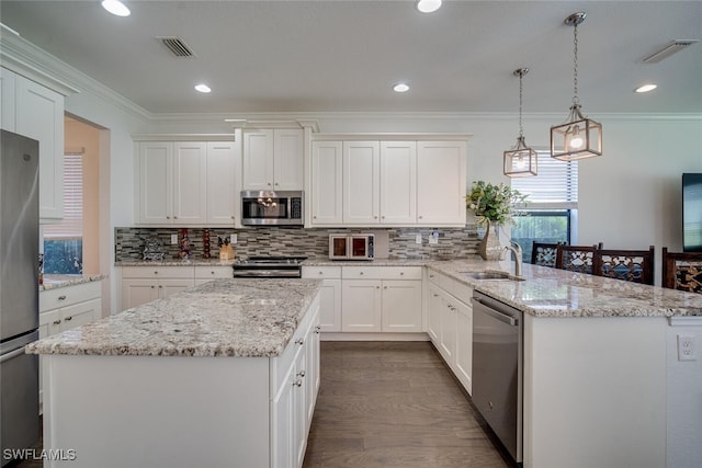 kitchen with hanging light fixtures, a kitchen island, appliances with stainless steel finishes, white cabinetry, and sink