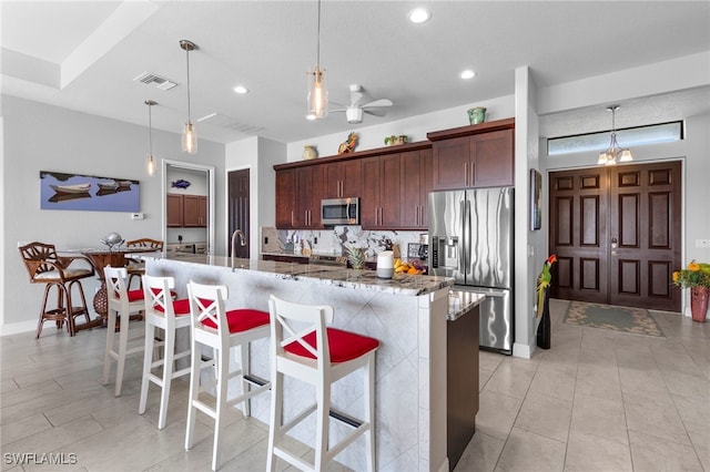 kitchen featuring a center island with sink, appliances with stainless steel finishes, a breakfast bar, dark stone counters, and pendant lighting