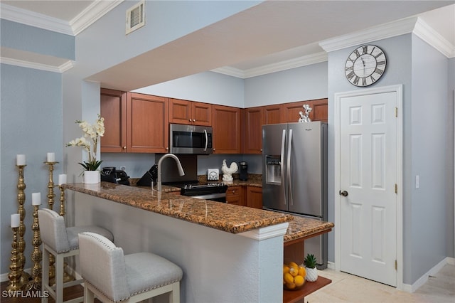 kitchen with appliances with stainless steel finishes, kitchen peninsula, dark stone countertops, ornamental molding, and a breakfast bar area