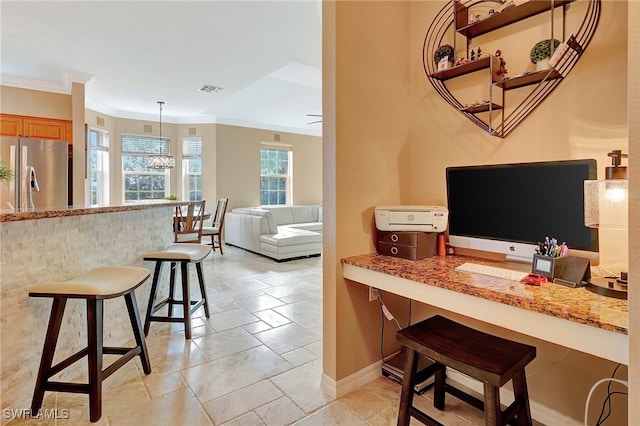 interior space featuring pendant lighting, light stone countertops, ornamental molding, a kitchen bar, and stainless steel refrigerator