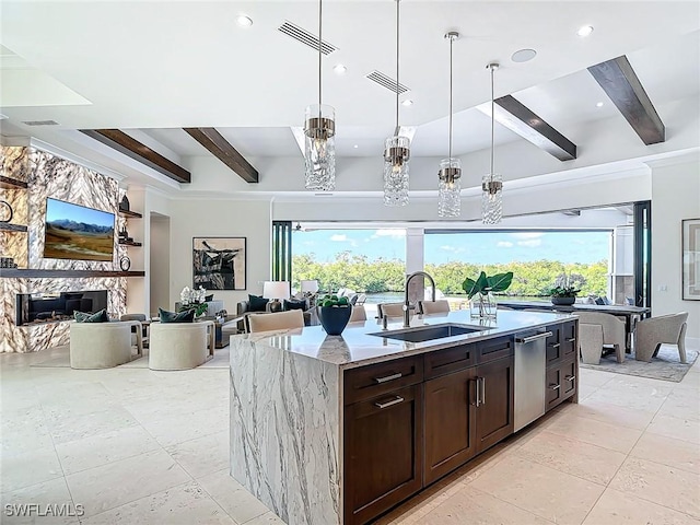 kitchen with sink, beam ceiling, light stone countertops, and a center island with sink