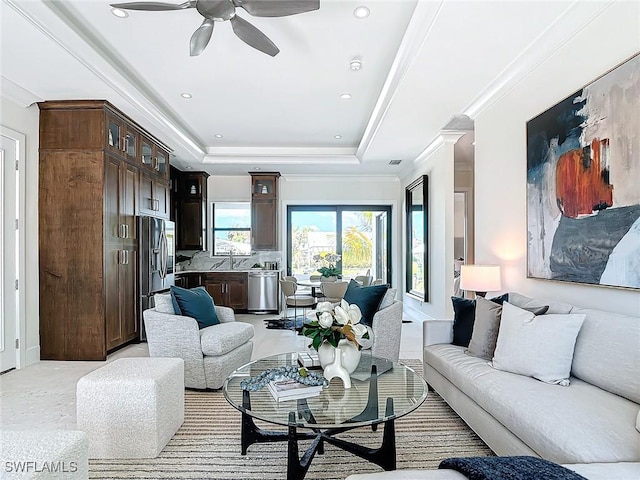 living room featuring sink, ceiling fan, a tray ceiling, crown molding, and light carpet