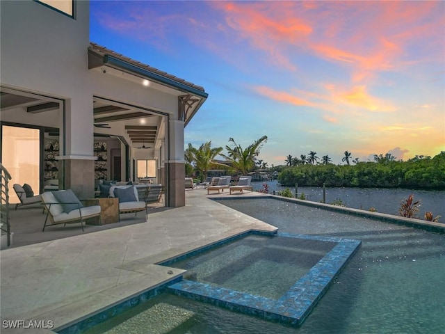 pool at dusk with an in ground hot tub, a water view, and a patio