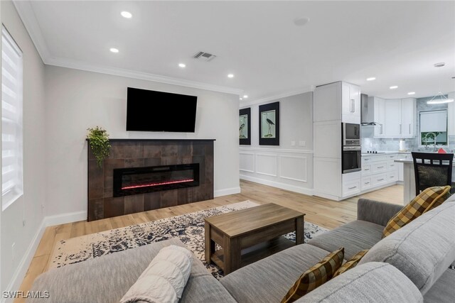 living room with crown molding, light wood-type flooring, and a tile fireplace