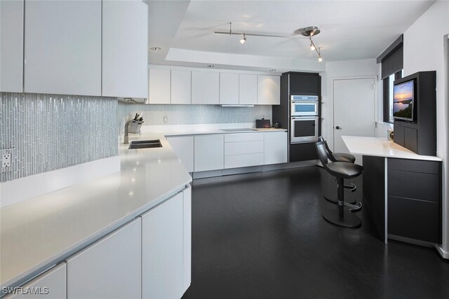 kitchen with sink, decorative backsplash, black electric cooktop, double oven, and white cabinetry