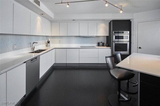 kitchen with sink, tasteful backsplash, a kitchen bar, white cabinets, and appliances with stainless steel finishes