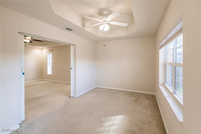 unfurnished room featuring ceiling fan, a healthy amount of sunlight, a raised ceiling, and light colored carpet