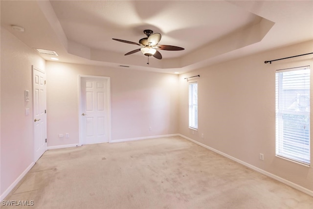 empty room with light carpet, a tray ceiling, and ceiling fan