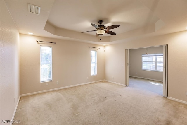 spare room with light carpet, a raised ceiling, and ceiling fan