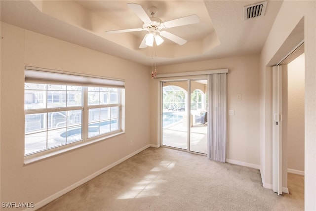 carpeted empty room with ceiling fan and a raised ceiling