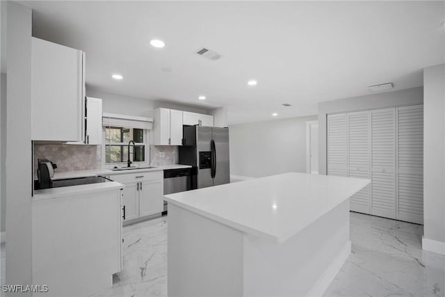 kitchen featuring sink, decorative backsplash, appliances with stainless steel finishes, a kitchen island, and white cabinetry