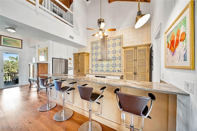 kitchen featuring visible vents, light stone counters, a high ceiling, light wood-type flooring, and wall chimney range hood