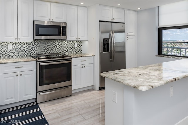 kitchen with white cabinets, tasteful backsplash, light stone counters, a kitchen island, and stainless steel appliances