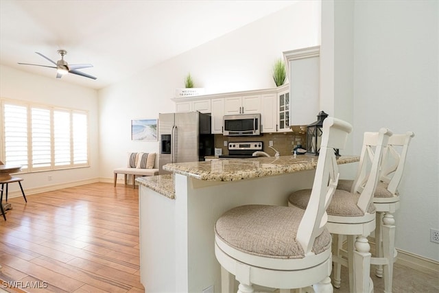 kitchen featuring a breakfast bar area, kitchen peninsula, white cabinetry, appliances with stainless steel finishes, and light hardwood / wood-style floors