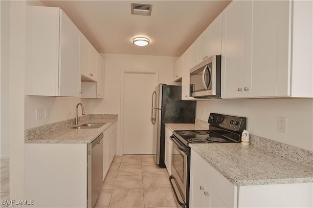 kitchen featuring sink, light stone countertops, white cabinets, light tile patterned floors, and appliances with stainless steel finishes