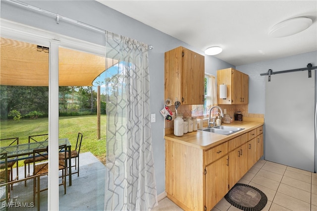 kitchen featuring sink, a barn door, decorative backsplash, and light tile patterned floors