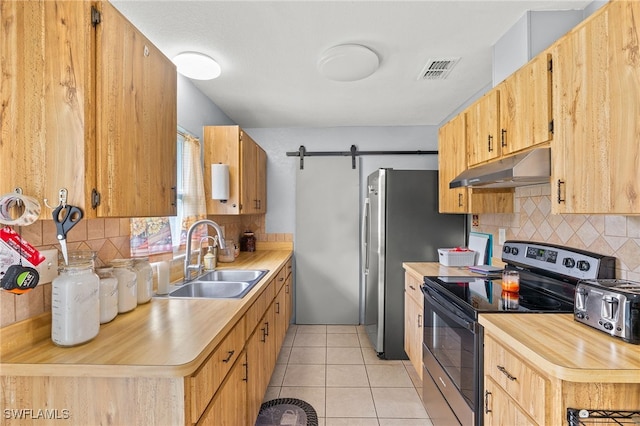 kitchen featuring tasteful backsplash, appliances with stainless steel finishes, light tile patterned flooring, sink, and a barn door