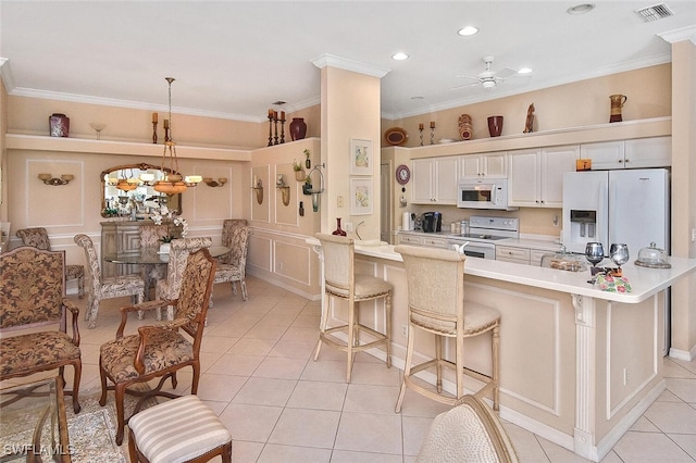 kitchen with white appliances, a kitchen breakfast bar, hanging light fixtures, white cabinets, and crown molding