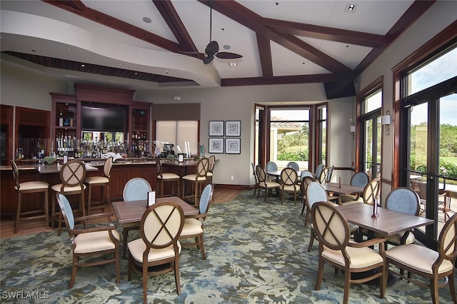 dining room featuring beamed ceiling, bar area, wood-type flooring, and high vaulted ceiling