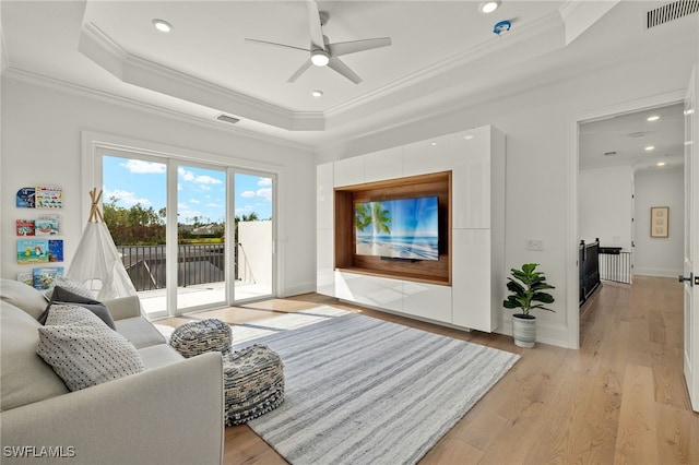 living room with ornamental molding, a tray ceiling, light wood-type flooring, and ceiling fan