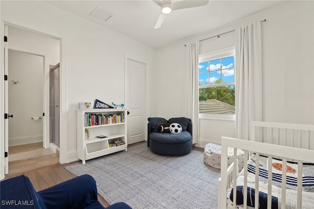 bedroom with hardwood / wood-style floors, a nursery area, and ceiling fan