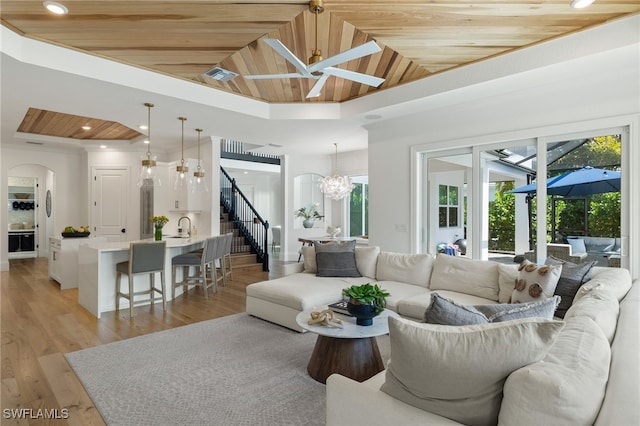 living room featuring lofted ceiling, wooden ceiling, light wood-type flooring, ceiling fan with notable chandelier, and sink