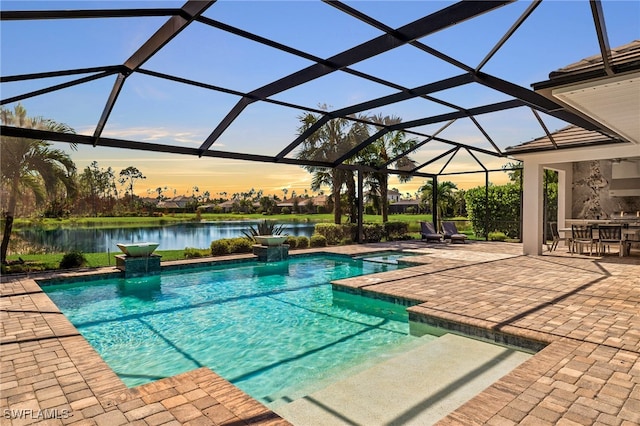 pool at dusk featuring a patio area, a lanai, an in ground hot tub, and a water view