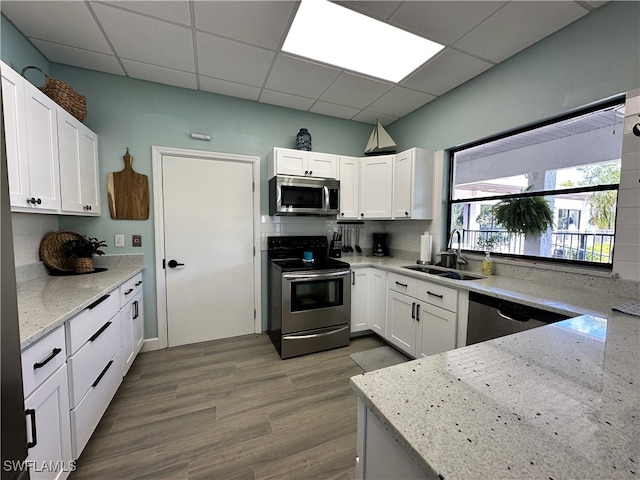 kitchen with hardwood / wood-style flooring, sink, white cabinets, appliances with stainless steel finishes, and light stone counters