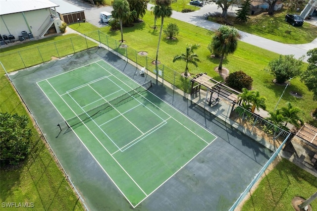 view of tennis court with a lawn and fence